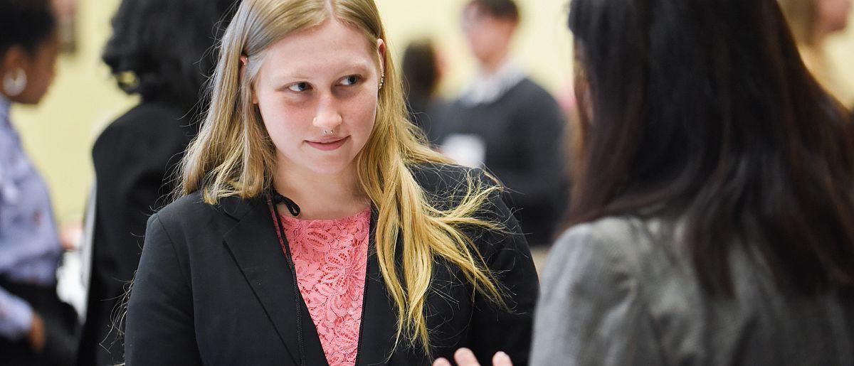 Image of student in business suite talking to another person looking away from the camera.